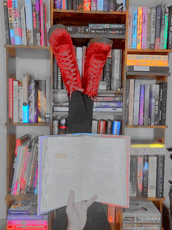 Blair reads with his red shoes up on his bookshelf full of books.